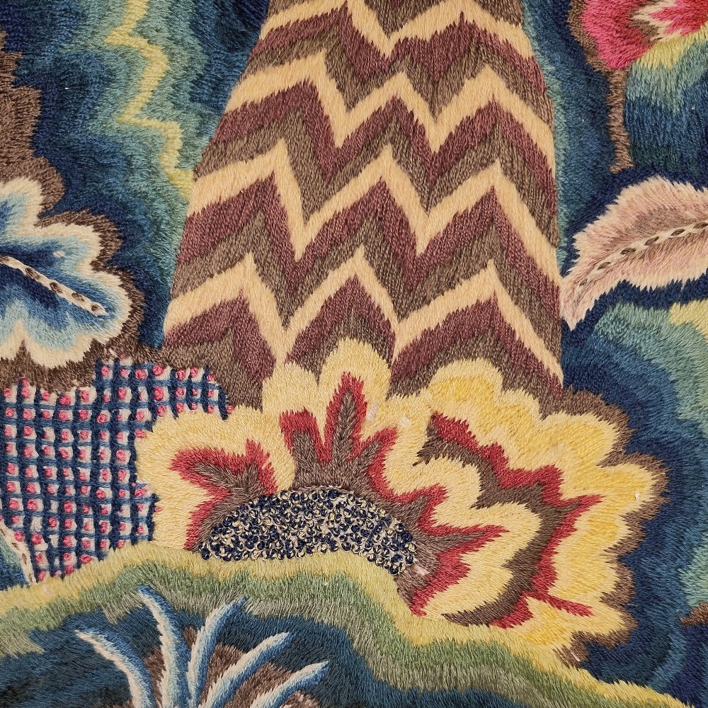 A long horizontal rectangular panel of hand-embroidered English crewelwork featuring stylised green foliage, pink blossoms, and undulating hillocks on a light linen ground. View IV