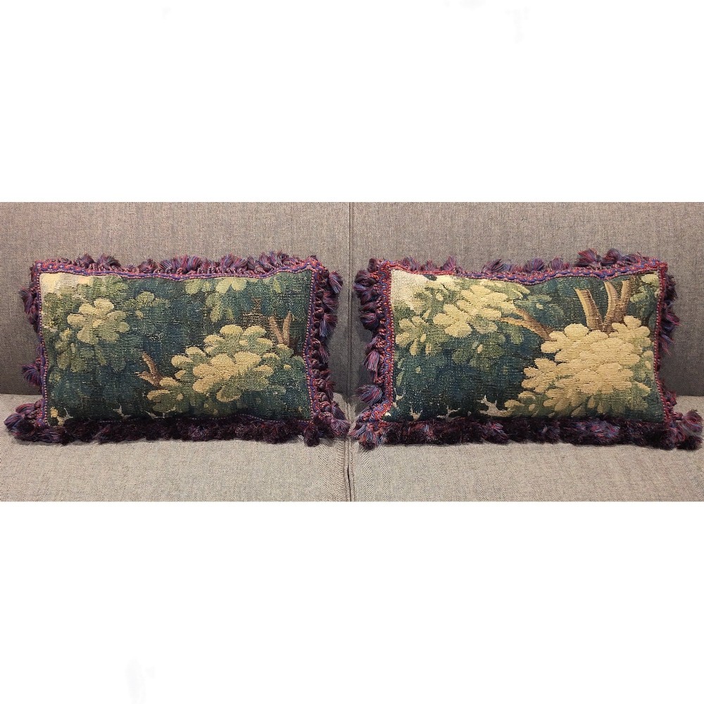 A pair of rectangular antique Aubusson verdure tapestry cushions featuring woven green botanical foliage and purple fringe edging.