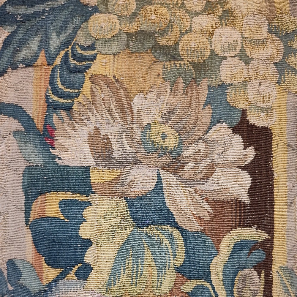 A rectangular cushion made from a seventeenth-century Flemish tapestry border featuring woven floral motifs, framed with a dark blue fringe. View III