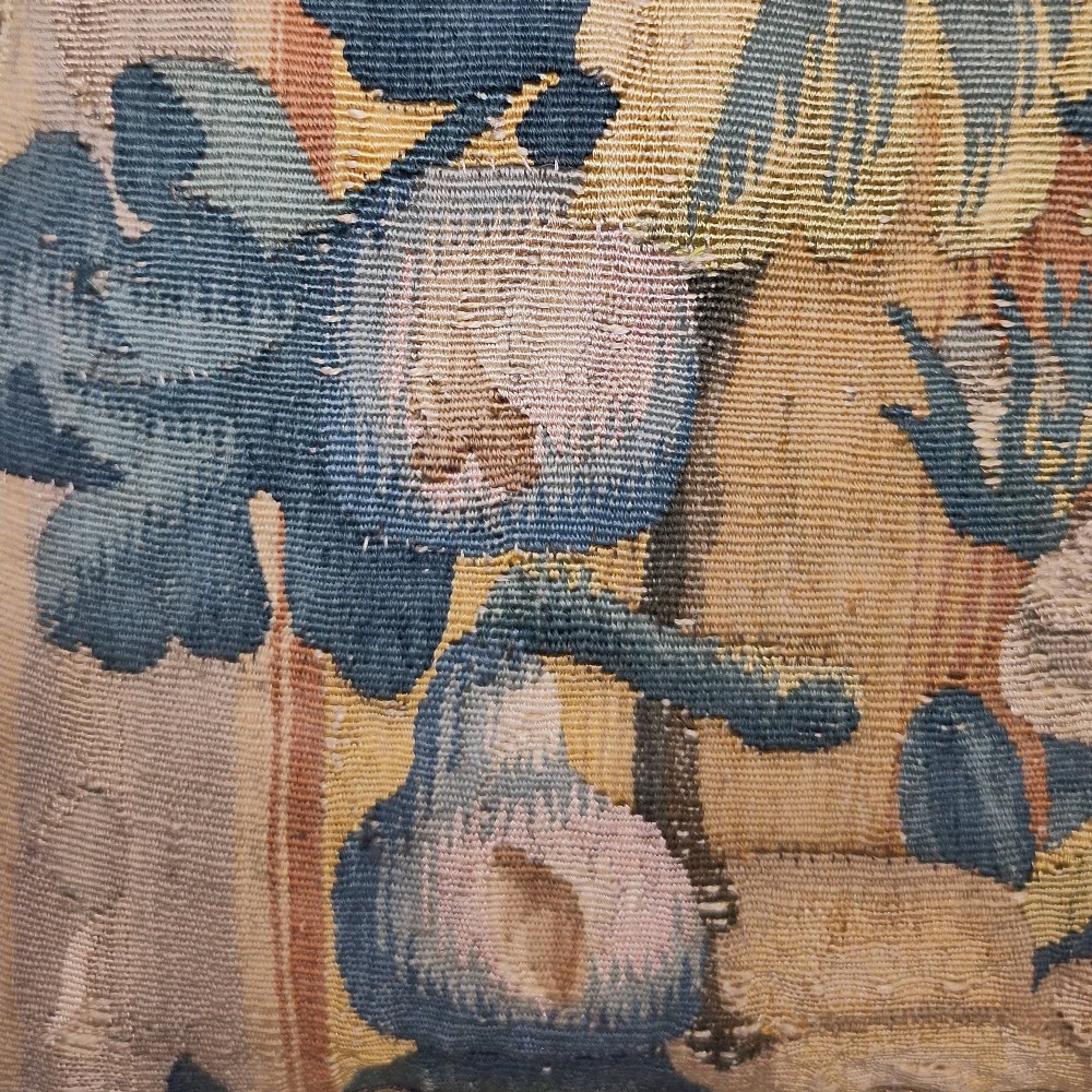 A rectangular cushion made from a seventeenth-century Flemish tapestry border featuring woven floral motifs, framed with a dark blue fringe. View IV