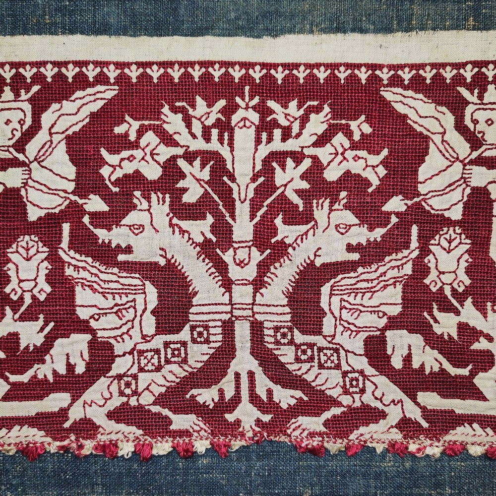 A horizontal 17th-century Italian embroidered red and cream linen border depicting winged figures and mythological creatures, mounted on blue backing within a carved gilt frame. View II