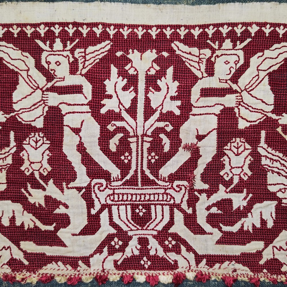 A horizontal 17th-century Italian embroidered red and cream linen border depicting winged figures and mythological creatures, mounted on blue backing within a carved gilt frame. View III
