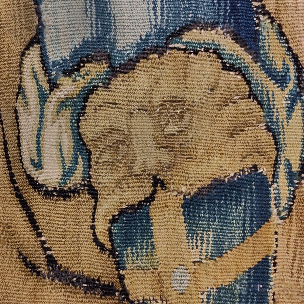 A vertical 16th century Flemish tapestry panel depicting a seated bearded male figure wearing a tall hat and draped robes in blue and gold tones. View IV