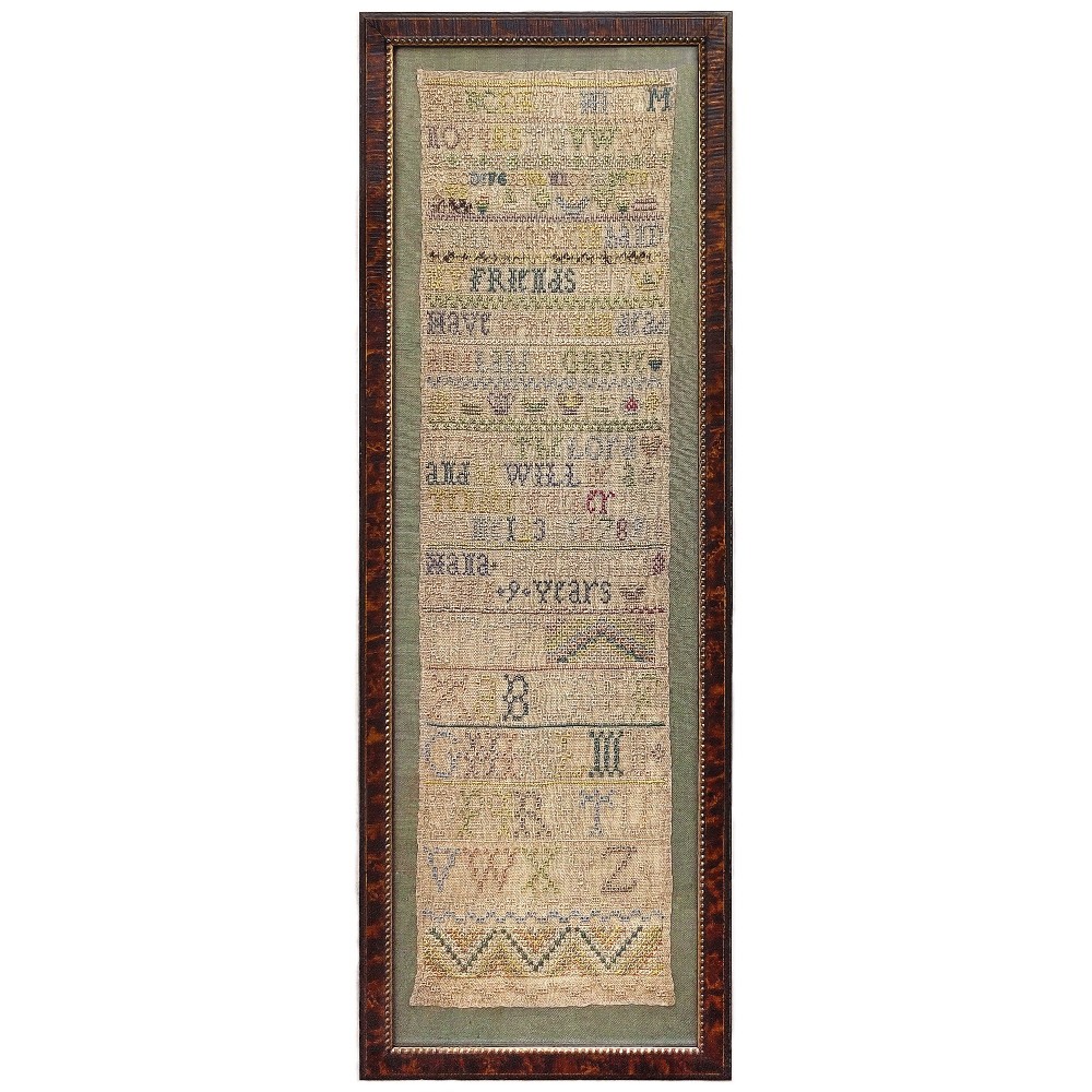 An 18th-century framed long narrow linen band sampler with rows of hand-embroidered alphabets, numbers, and geometric stitch patterns.