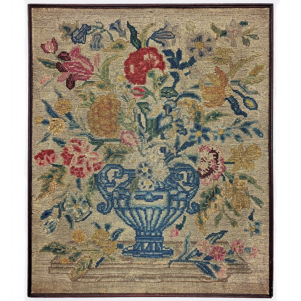 A framed 18th-century English needlework panel featuring a vase of multi-coloured flowers hand-stitched on a beige ground.