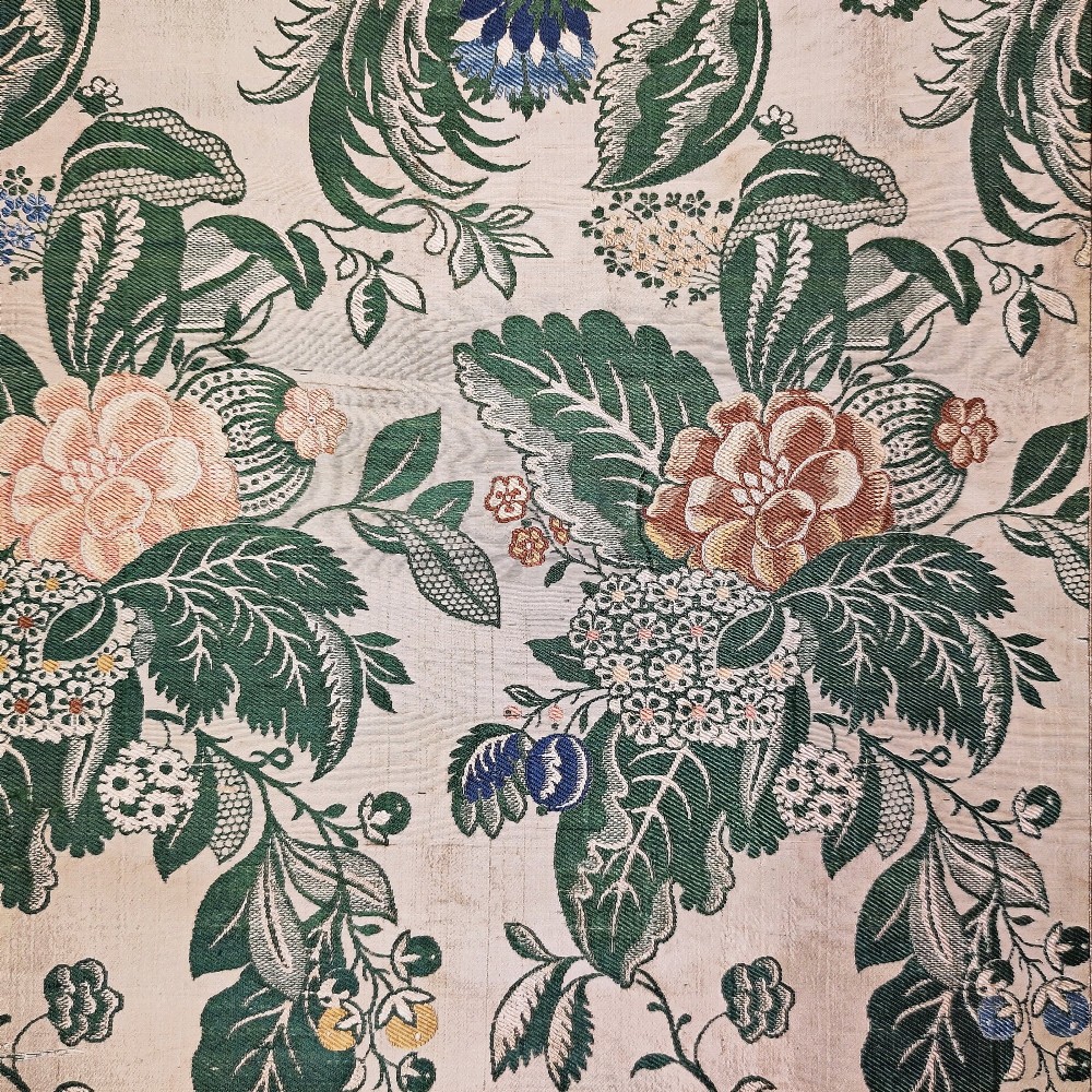 An 18th-century floral woven Spitalfields silk panel with green leaves and pastel blossoms, presented inside a dark wood rectangular frame. View II