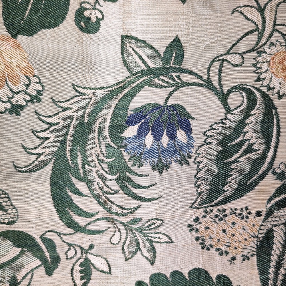An 18th-century floral woven Spitalfields silk panel with green leaves and pastel blossoms, presented inside a dark wood rectangular frame. View III