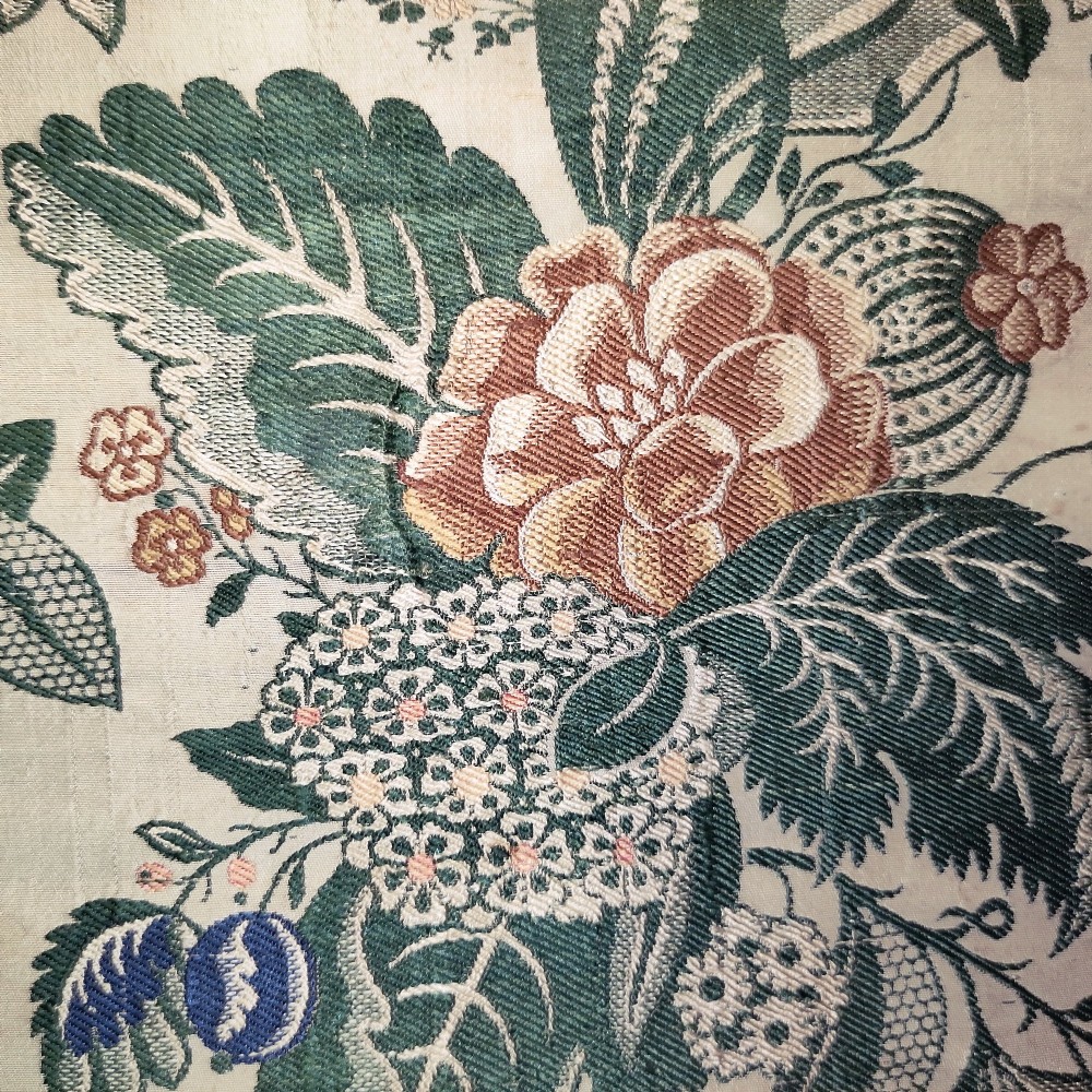 An 18th-century floral woven Spitalfields silk panel with green leaves and pastel blossoms, presented inside a dark wood rectangular frame. View IV