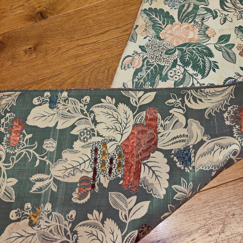 An 18th-century floral woven Spitalfields silk panel with green leaves and pastel blossoms, presented inside a dark wood rectangular frame. View VI