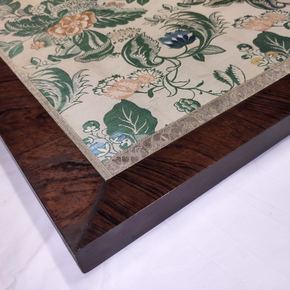 An 18th-century floral woven Spitalfields silk panel with green leaves and pastel blossoms, presented inside a dark wood rectangular frame. View VII