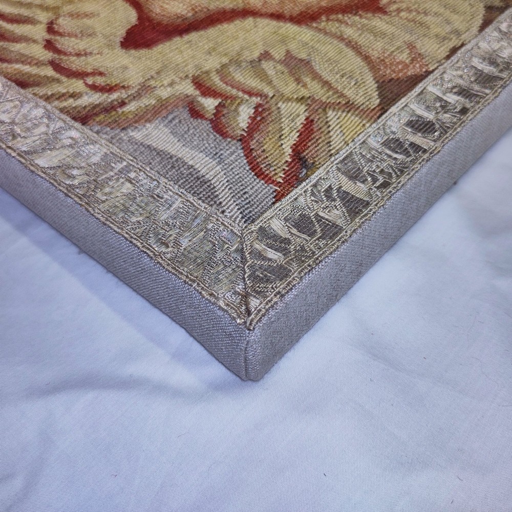 A vertical rectangular 17th-century tapestry fragment featuring a winged cherub head and scrolling acanthus motifs framed by a woven border. View II