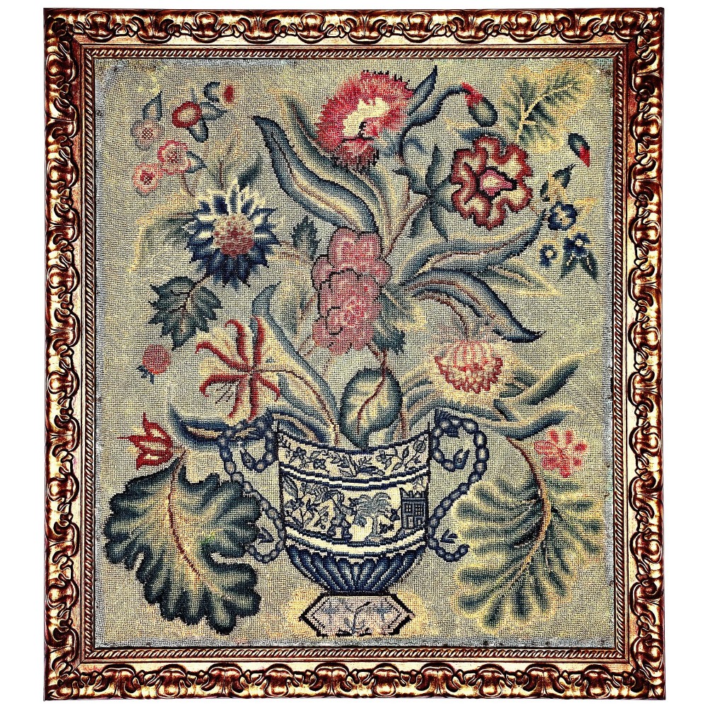 An 18th-century framed needlework picture depicting a floral arrangement in an urn within a carved giltwood frame.