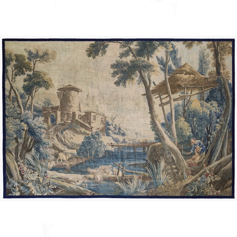 An eighteenth-century Aubusson hand-woven tapestry depicting a pastoral landscape with a river, stone tower, thatched structure, and figures in shades of blue, green, and beige.