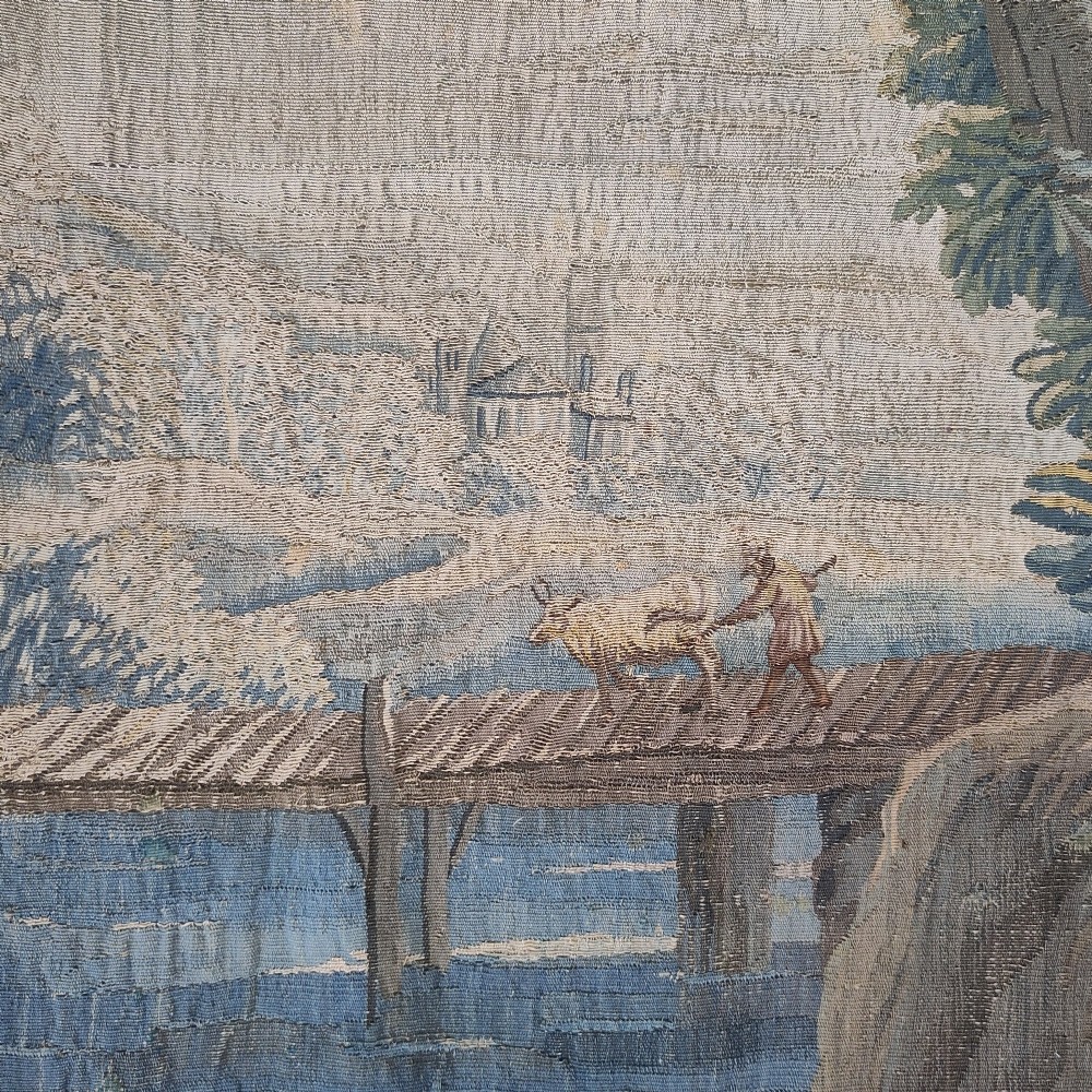 An eighteenth-century Aubusson hand-woven tapestry depicting a pastoral landscape with a river, stone tower, thatched structure, and figures in shades of blue, green, and beige. View V