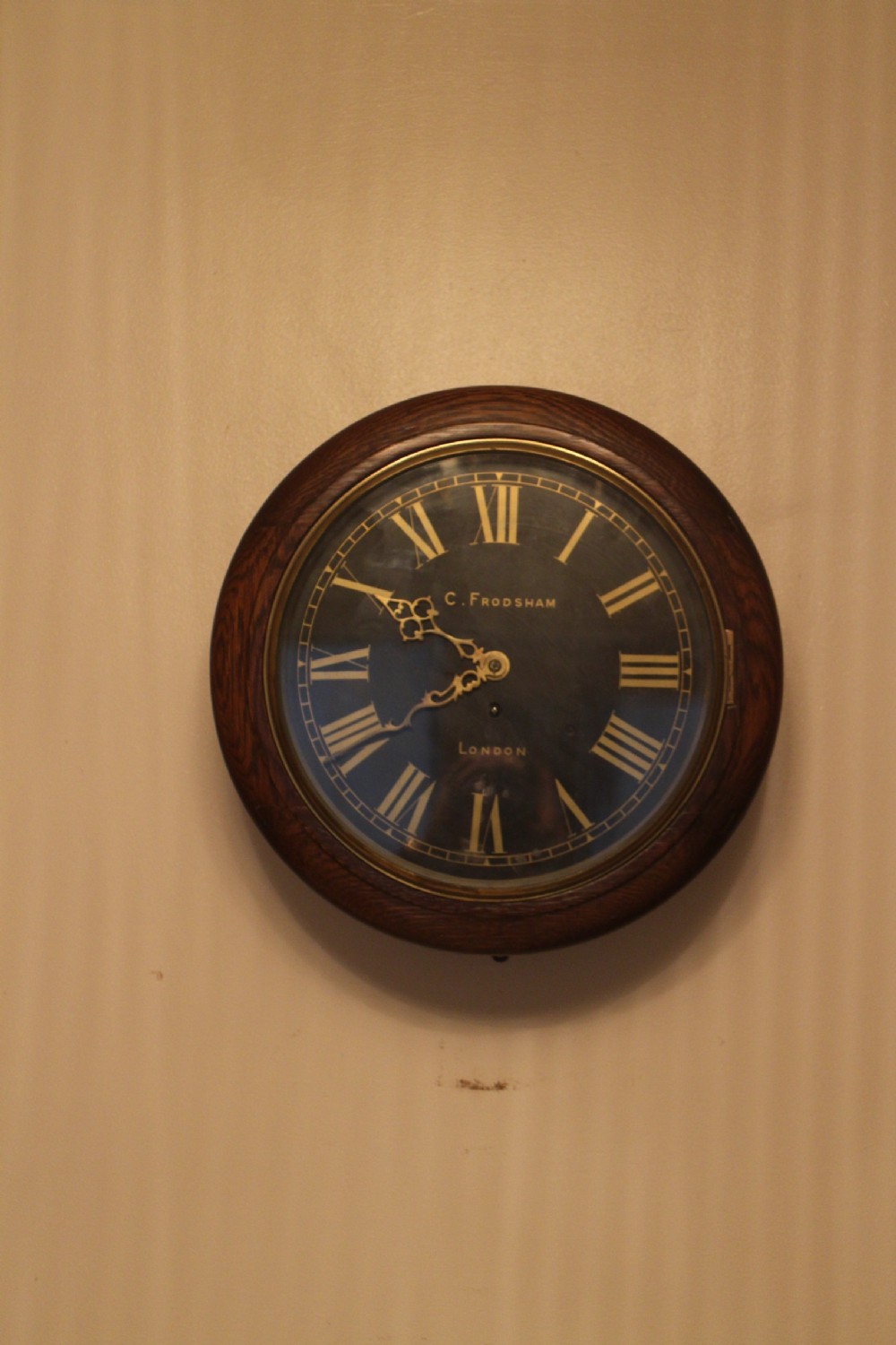 A circular Victorian fusee dial clock featuring a dark wood surround, a black dial signed C. Frodsham London with gilt Roman numerals, and ornate brass hands.