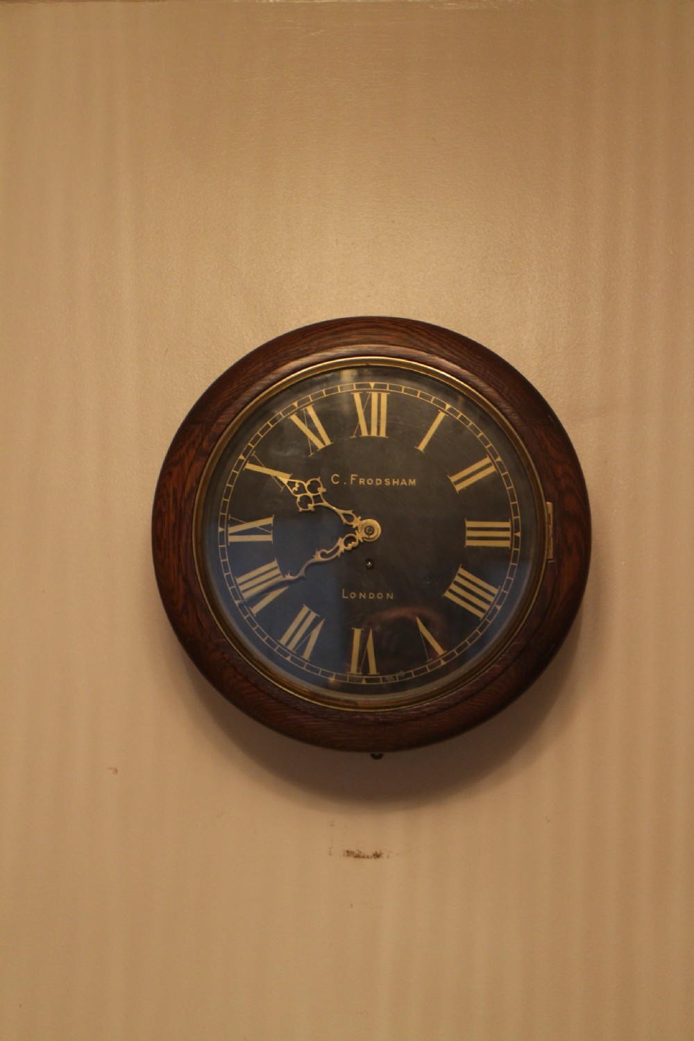 A circular Victorian fusee dial clock featuring a dark wood surround, a black dial signed C. Frodsham London with gilt Roman numerals, and ornate brass hands. View II