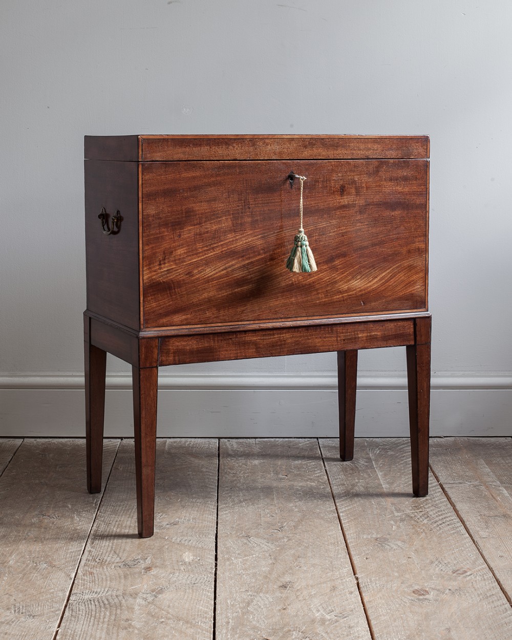 A Georgian mahogany cellaret on tapered square legs with flame mahogany grain on the front, brass side handles, and a key with a green tassel.