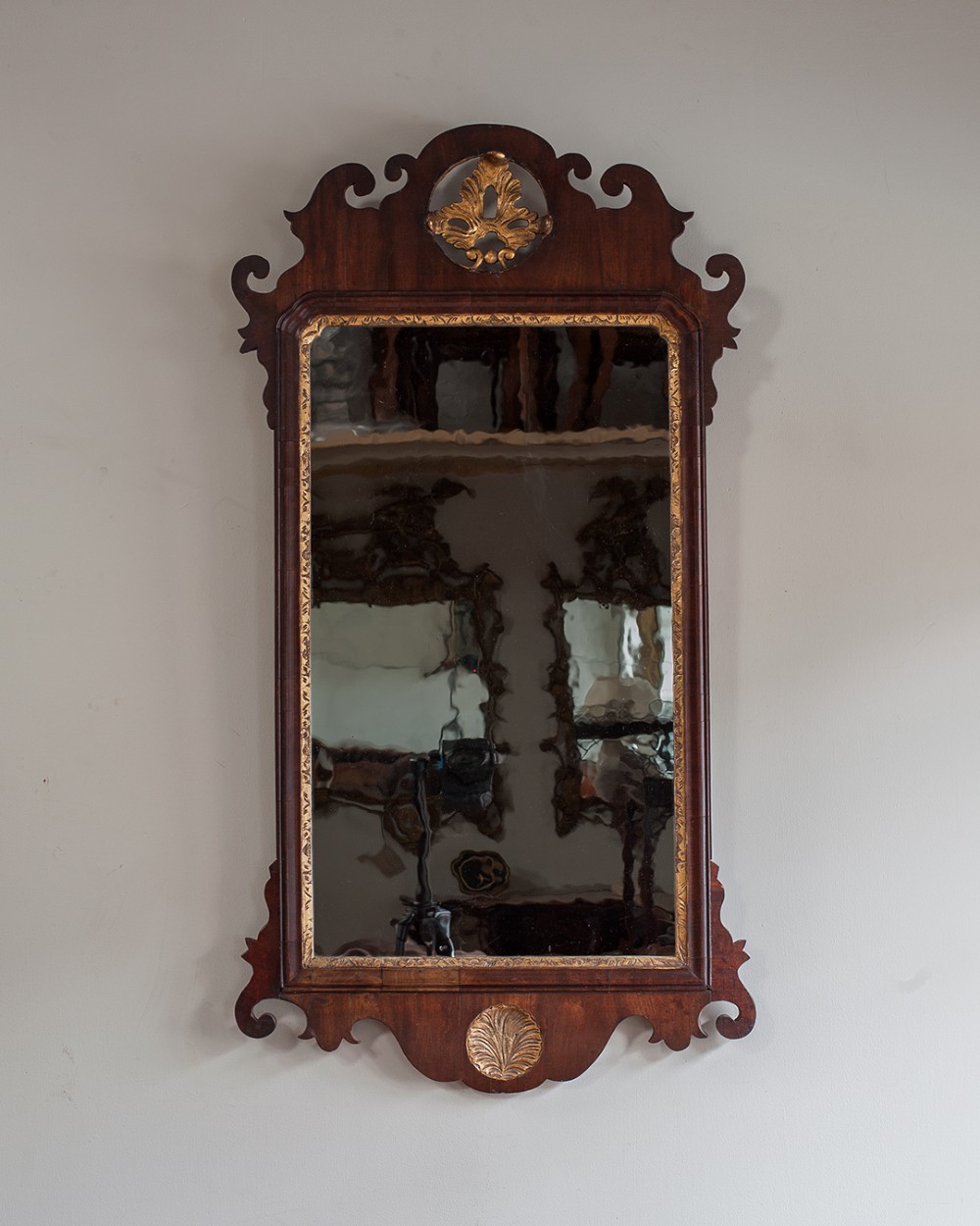 A Georgian mahogany fretwork wall mirror featuring scroll-cut edges, a gilded interior rim, a gilt medallion crest at the top, and a carved shell emblem at the base.
