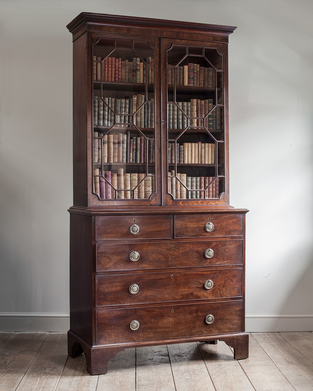 A George III dark mahogany cabinet on chest featuring upper glazed doors with geometric astragal bars above a four-drawer base raised on bracket feet.