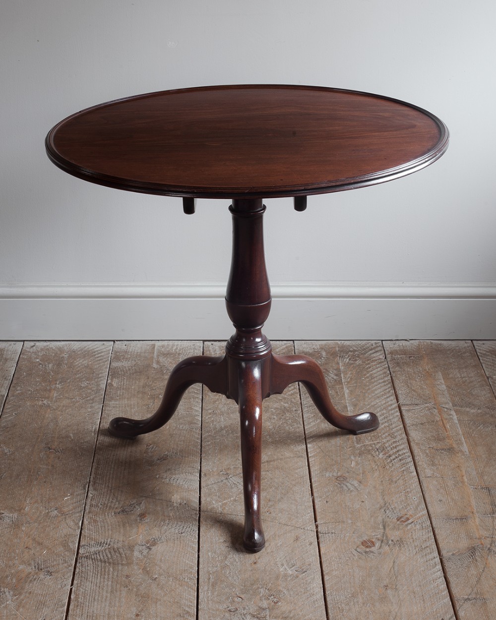 A Georgian mahogany tripod table featuring an oval top with a moulded rim resting on a turned central column and three down-swept cabriole legs.