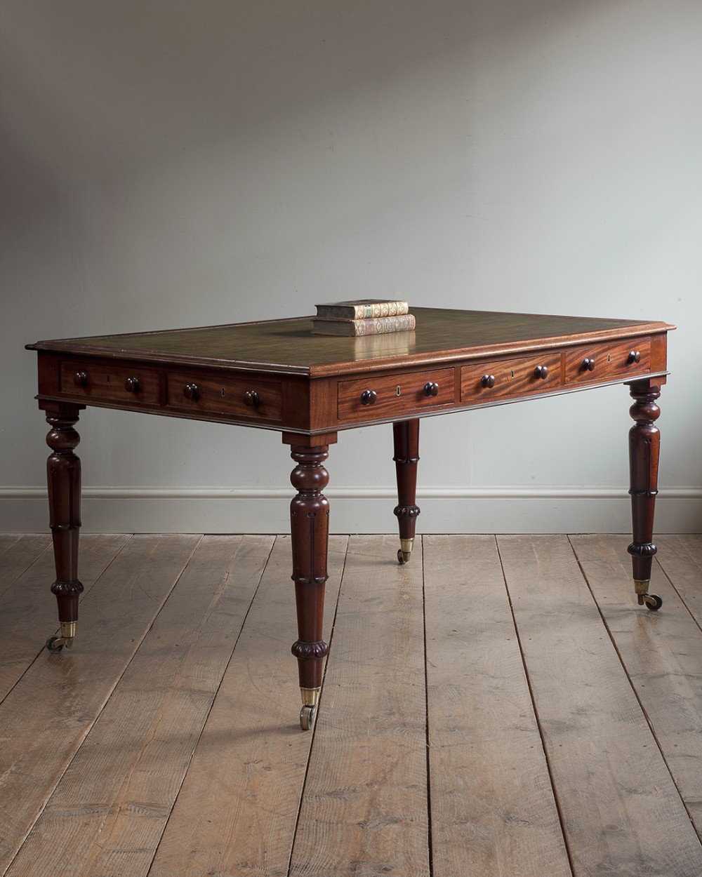 A 19th-century mahogany library table featuring a green leather inset top, frieze drawers with wooden knobs, and four turned legs with brass castors.