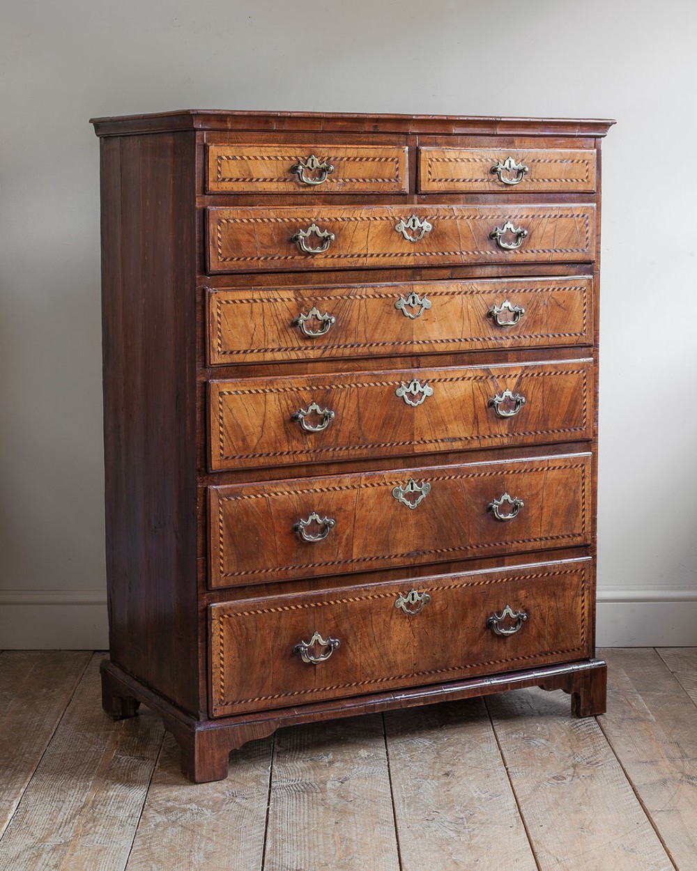 A tall Georgian walnut chest of drawers with herringbone inlay, brass handles, and bracket feet.