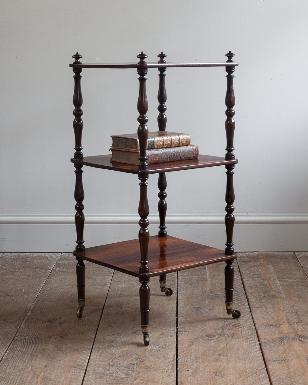 A small three-tiered William IV rosewood whatnot featuring turned corner pillars, top finials, and brass castors.