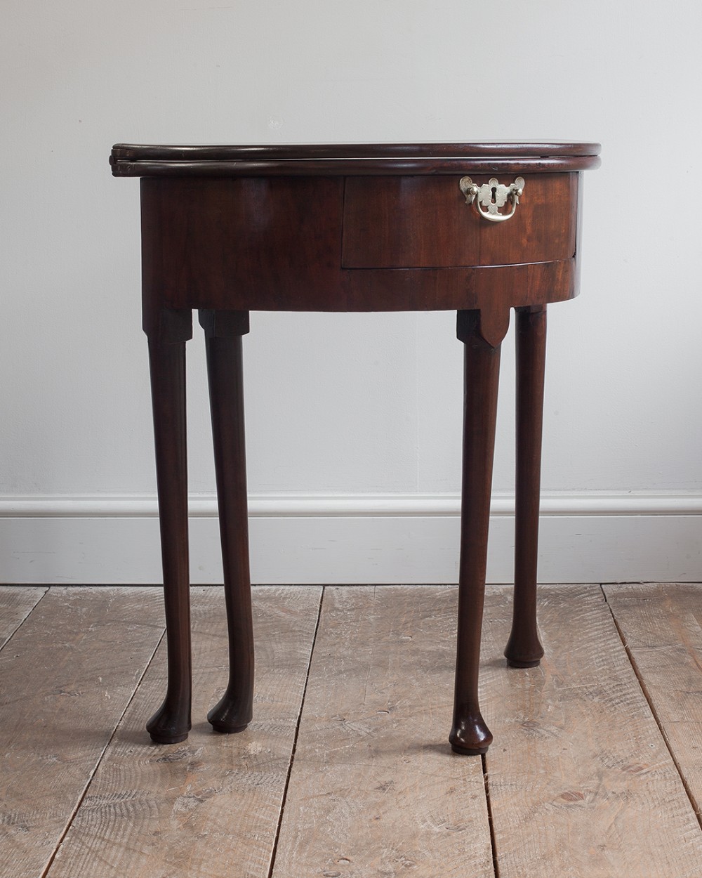 A George II Cuban mahogany demi-lune tea table featuring a fold-over hinged top, a frieze drawer with a brass keyhole escutcheon, and four slender legs ending in pad feet.