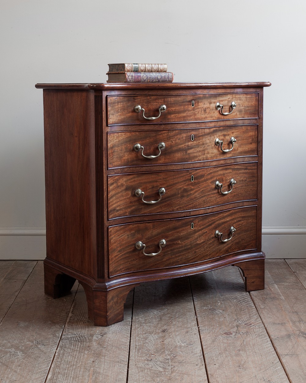 A compact George III mahogany chest of drawers with a serpentine front, four graduated drawers, brass handles, reeded corner pilasters, and bracket feet.