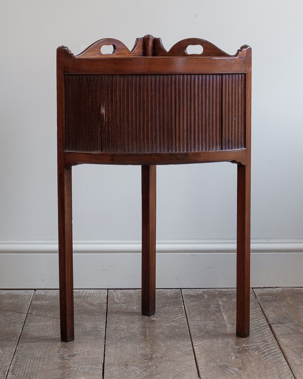 An antique Georgian mahogany corner cupboard featuring a reeded tambour door, shaped gallery with cutout handles, and three straight legs.
