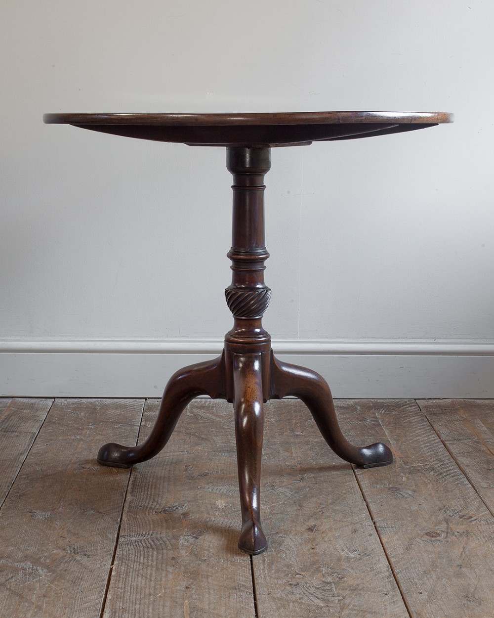 An antique Georgian dark mahogany tripod table featuring a circular top, a central turned pedestal with spiral carving, and three sweeping cabriole legs.