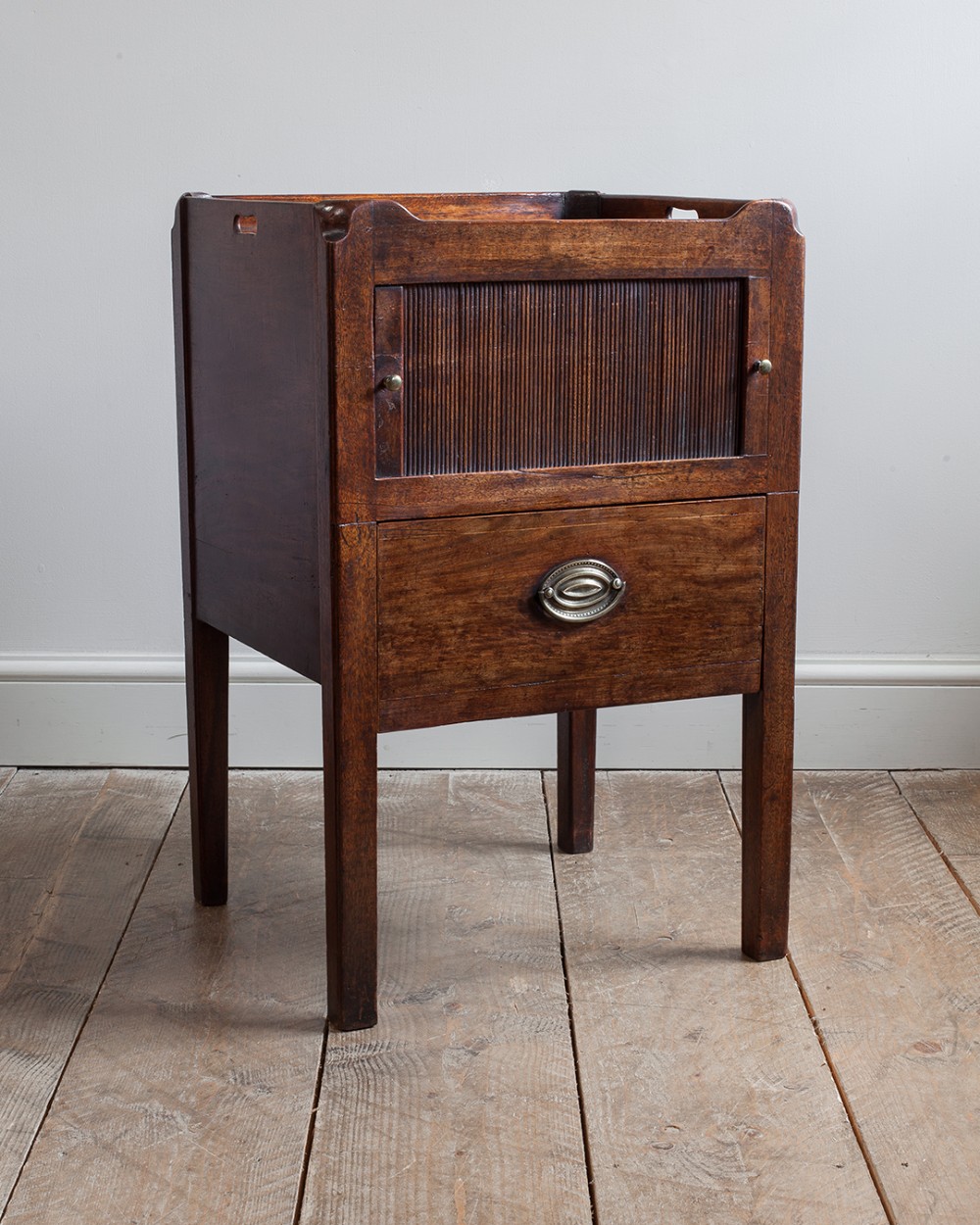 A George III mahogany nightstand featuring a gallery tray top with cutout handles, a slatted tambour door, and a lower drawer.