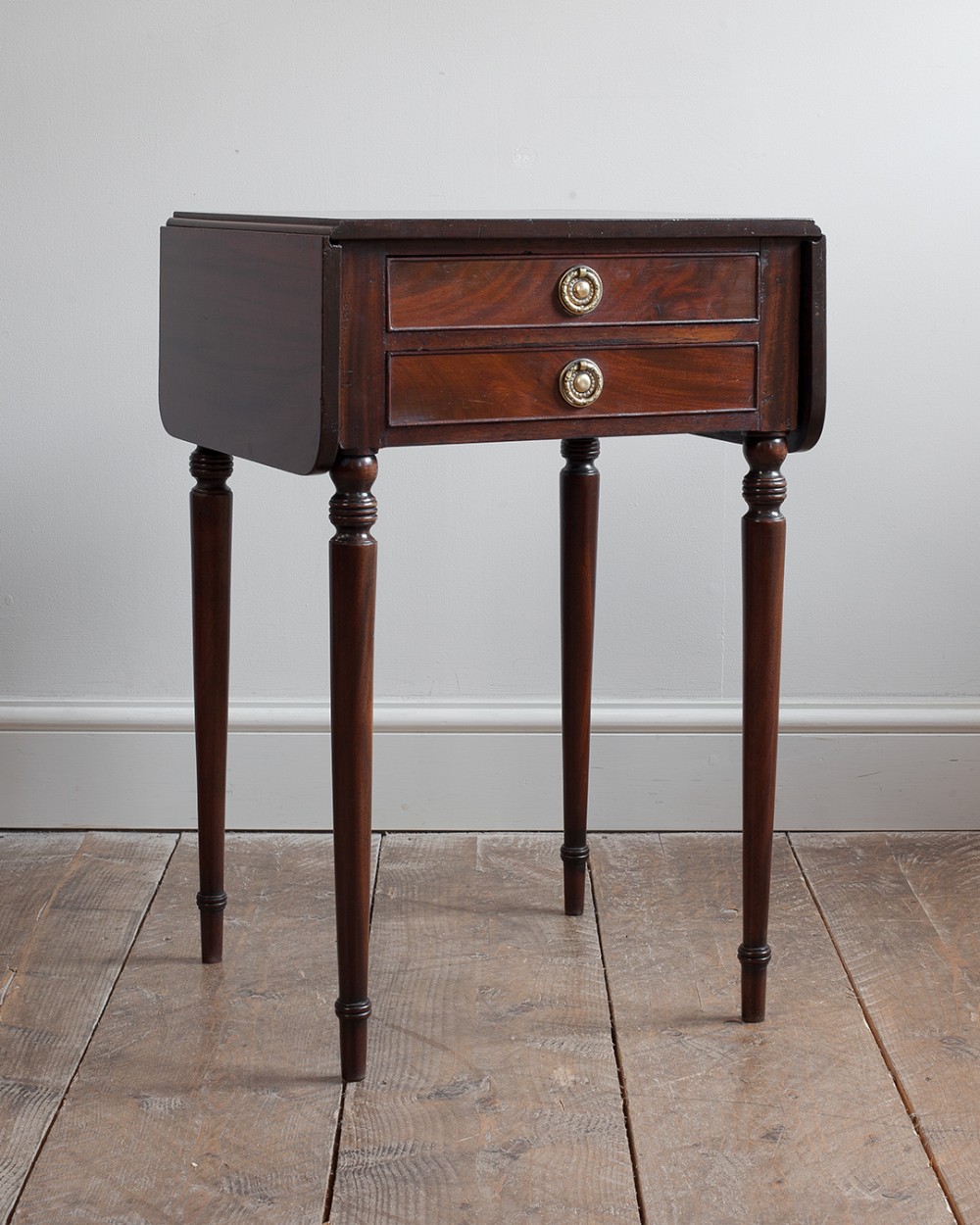 A Regency mahogany work table featuring two drawers with circular brass pull handles, drop-leaf sides, and tall turned legs.