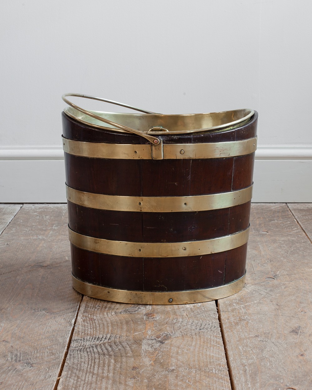 A 19th-century dark mahogany staved wood bucket bound with four horizontal brass bands, featuring a brass interior liner and a swing handle.