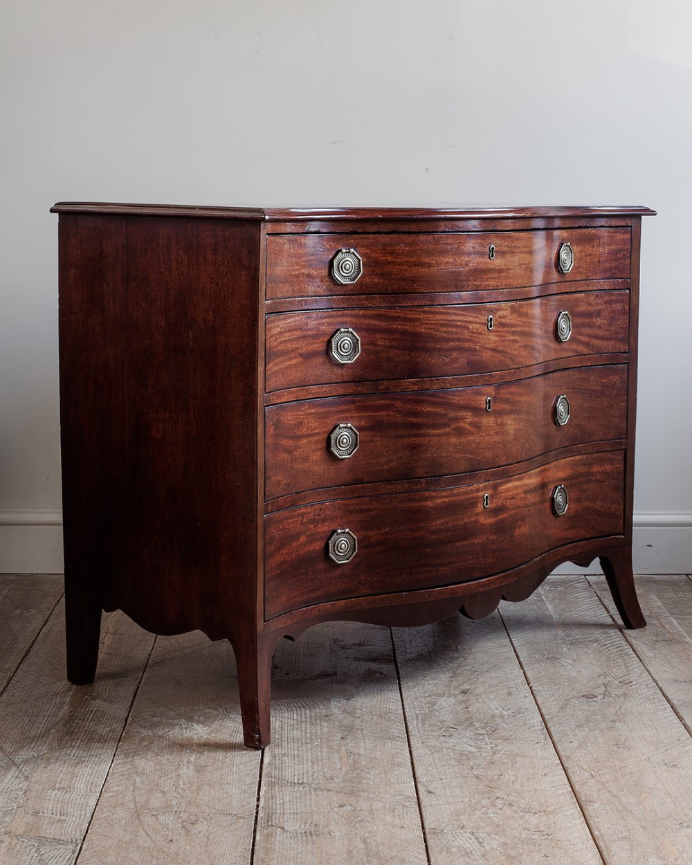A George III dark mahogany chest of drawers featuring a curved serpentine front, four graduated drawers with octagonal brass handles, and bracket feet.
