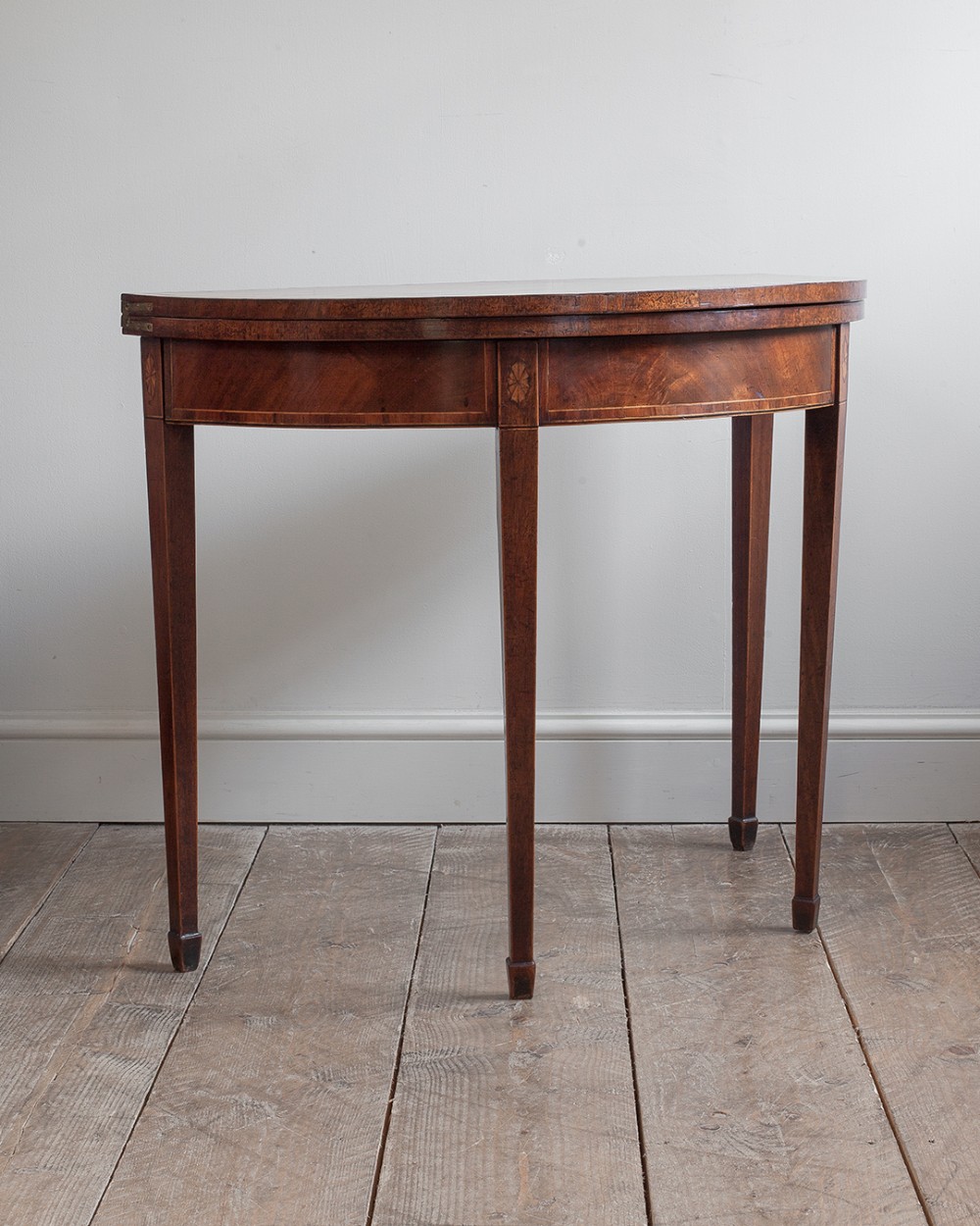 An 18th-century Georgian mahogany demi-lune card table featuring tapered legs, string inlay, and a hinged fold-over top.