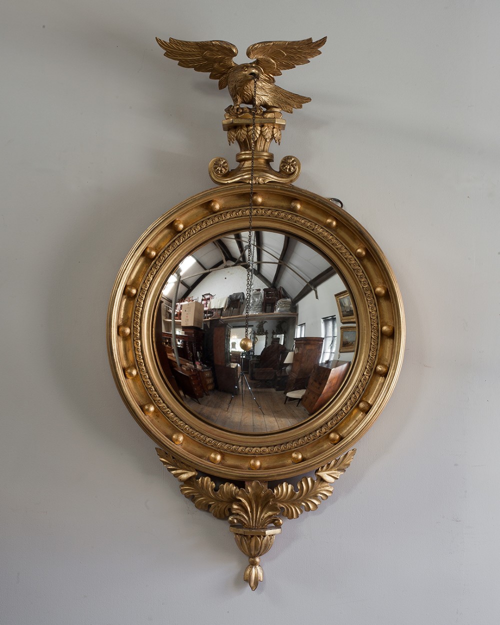 A circular Regency giltwood convex mirror topped with a carved eagle surmount and bordered with gilded spherules.