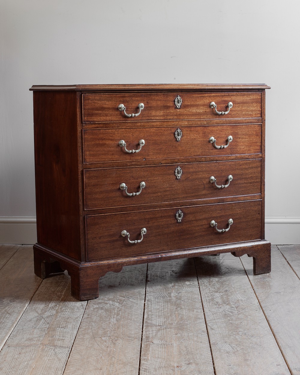 A George III mahogany chest of drawers featuring four graduated drawers with metal swan-neck handles and shaped bracket feet.