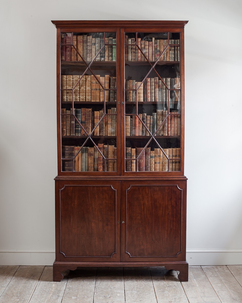 A tall Georgian mahogany library bookcase featuring two astragal glazed upper doors above two solid panelled lower cupboard doors.