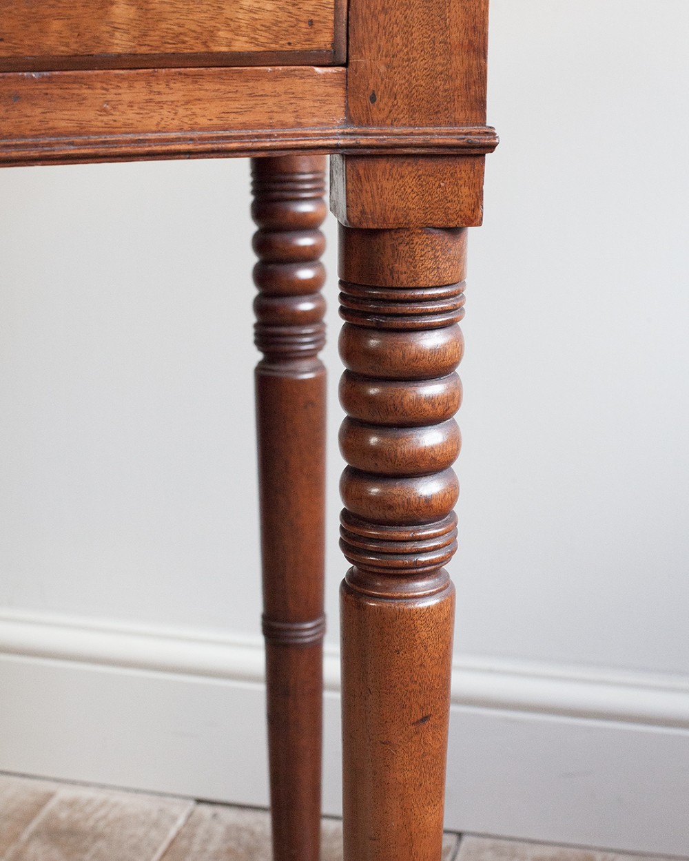 A nineteenth-century mahogany bowfront side table featuring a single drawer with two brass knobs and four ring-turned legs. View III