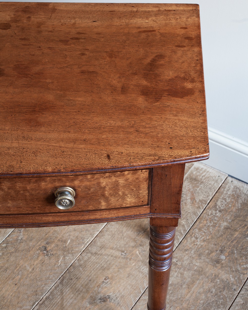 A nineteenth-century mahogany bowfront side table featuring a single drawer with two brass knobs and four ring-turned legs. View V