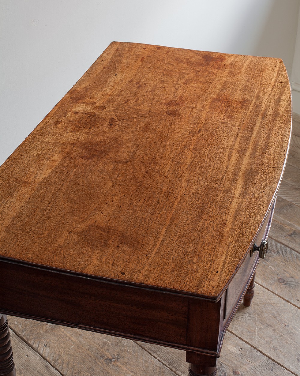 A nineteenth-century mahogany bowfront side table featuring a single drawer with two brass knobs and four ring-turned legs. View VI