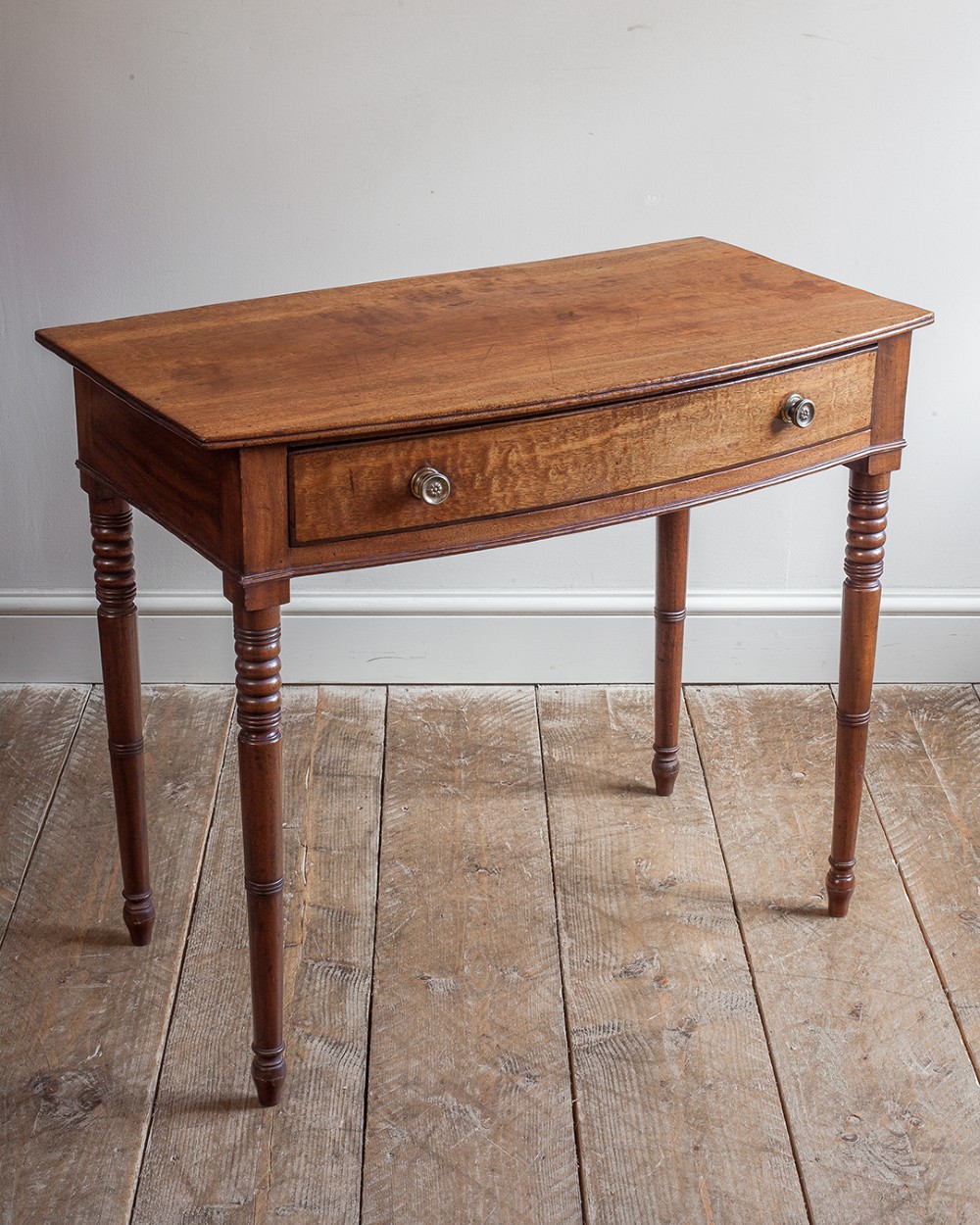 A nineteenth-century mahogany bowfront side table featuring a single drawer with two brass knobs and four ring-turned legs. View VII