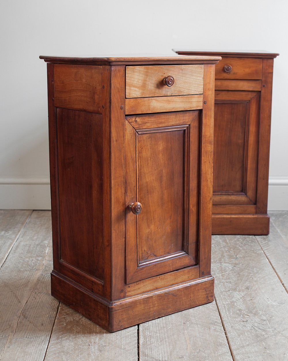 A pair of 19th-century French cherrywood bedside cupboards featuring single top drawers, panelled doors, turned timber knobs, and solid plinth bases. View VI