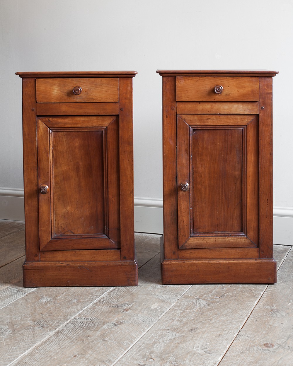 A pair of 19th-century French cherrywood bedside cupboards featuring single top drawers, panelled doors, turned timber knobs, and solid plinth bases. View VII