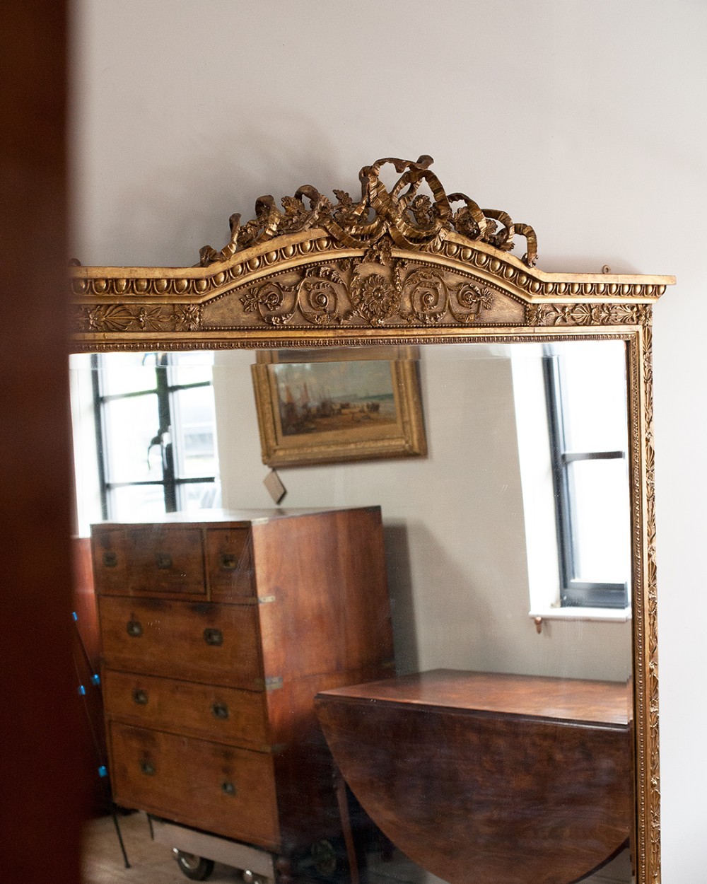 A large 19th-century rectangular giltwood overmantel mirror featuring a ribbon bow knot crest, carved bead moulding, and a flared base. View VI