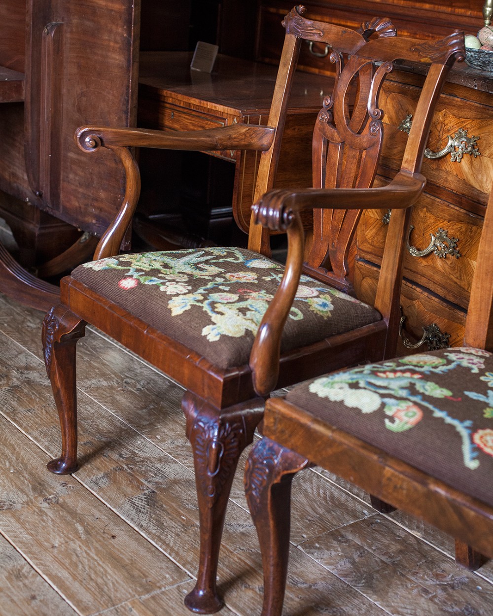 A set of twelve 18th-century carved walnut dining chairs featuring vase-shaped splats, cabriole legs, and floral needlepoint seats. View VI