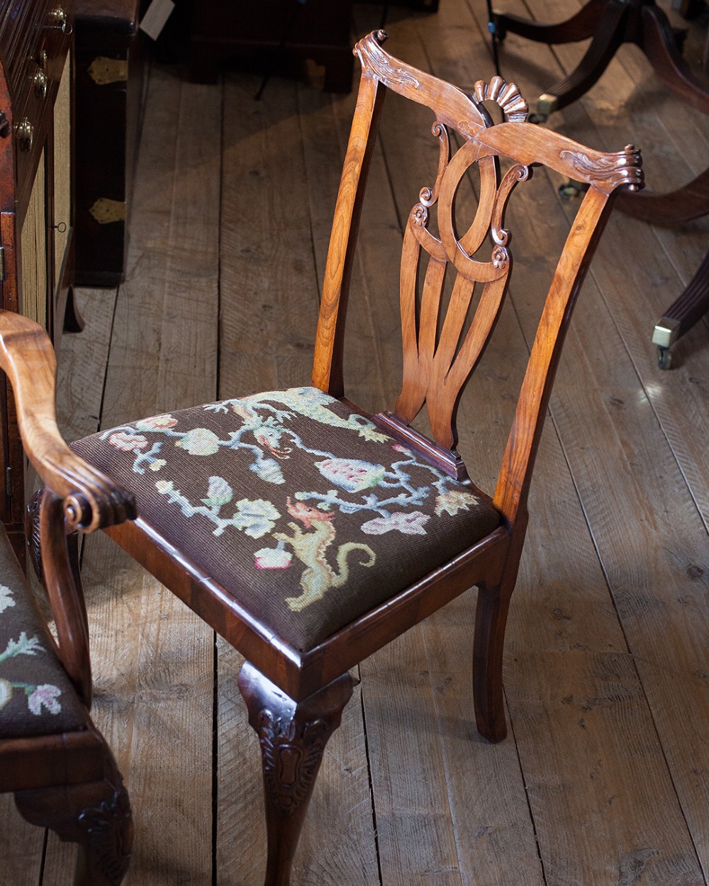 A set of twelve 18th-century carved walnut dining chairs featuring vase-shaped splats, cabriole legs, and floral needlepoint seats. View IX