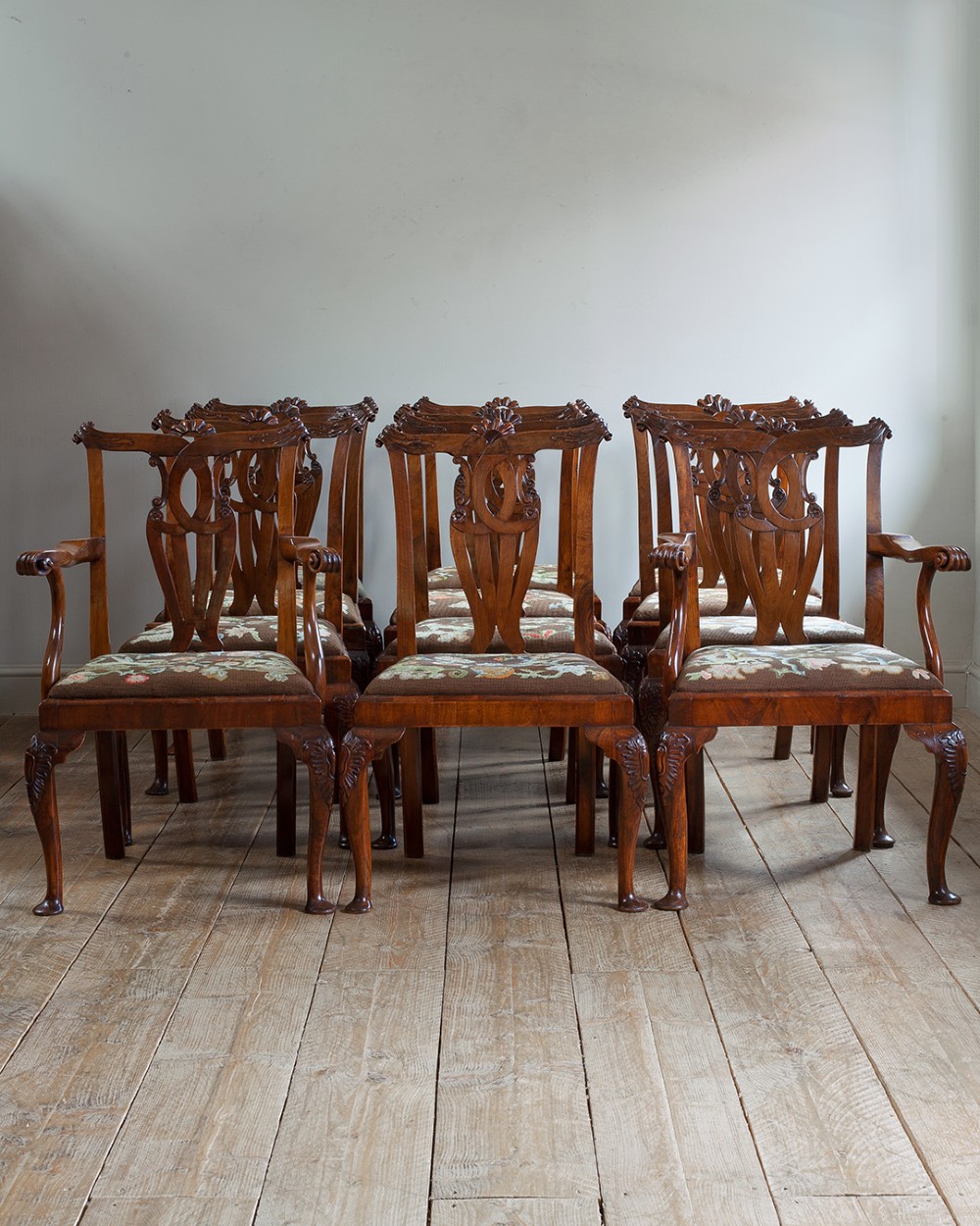 A set of twelve 18th-century carved walnut dining chairs featuring vase-shaped splats, cabriole legs, and floral needlepoint seats.