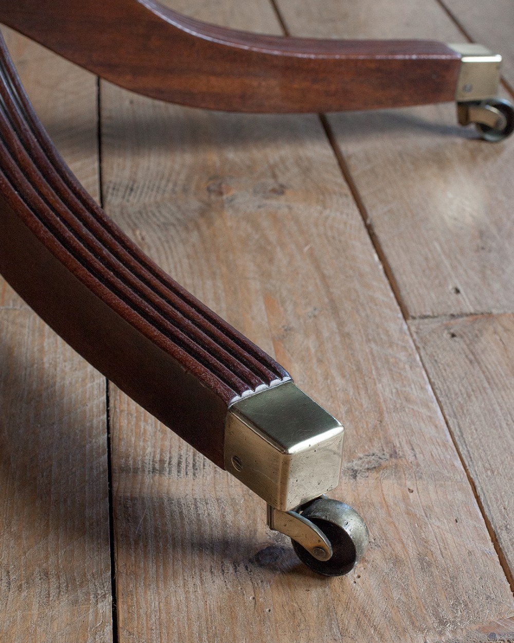 A Regency mahogany extending twin pedestal dining table with rounded corners, reeded splayed legs, and brass caps with castors. View II